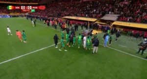 Les joueurs du Sénégal et du Maroc sont sur le terrain lors d'un match tendu, avec une foule vibrante en arrière-plan et le score toujours de 0-0.