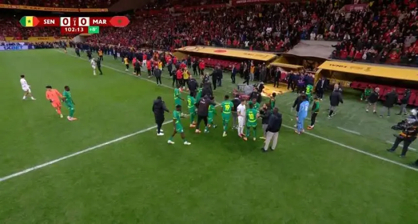 Les joueurs du Sénégal et du Maroc sont sur le terrain lors d'un match tendu, avec une foule vibrante en arrière-plan et le score toujours de 0-0.