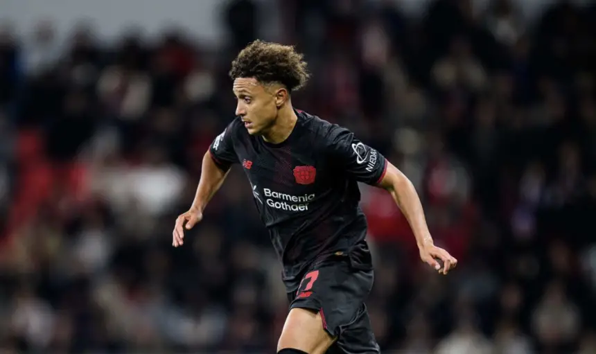 Moroccan footballer Amine Adli in action, wearing a dark jersey with red accents, during a match, showcasing his agility and focus.