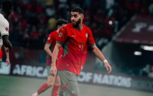 إسماعيل الصيباري بزي المنتخب المغربي، يواجه السنغال خلال كأس أمم أفريقيا، مع مشجعين وأجواء الملعب في الخلفية.