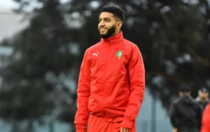 Ismaël Saibari smiles while wearing a red Moroccan national team tracksuit, preparing for the Africa Cup final.