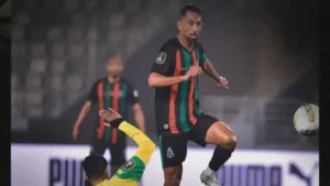 Een Marokkaanse speler in een gestreept groen-zwart tenue springt om de bal te controleren tijdens een intense wedstrijd tegen een tegenstander in een geel shirt.