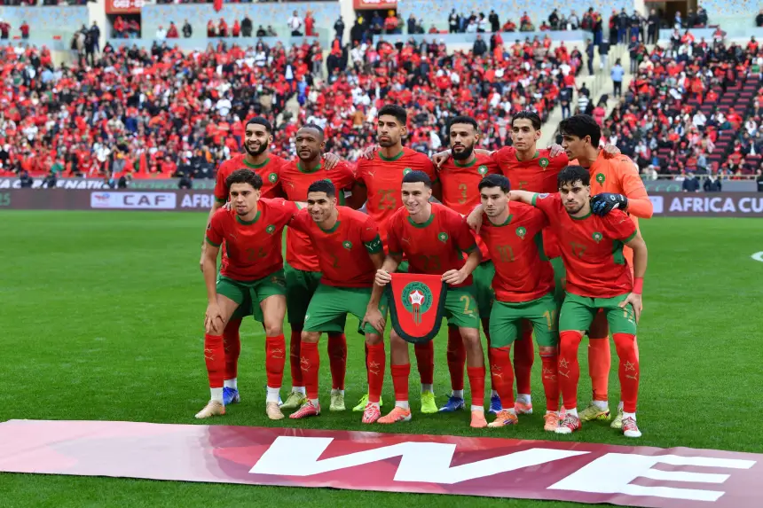 L'équipe nationale de football du Maroc pose pour une photo d'équipe dans des tenues rouge vif avec des accents verts, célébrant devant une foule vibrante.