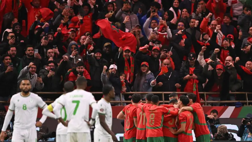 Des supporters marocains en rouge vif célèbrent tandis que les joueurs s'embrassent de joie après un but lors d'un match contre l'Algérie, reflétant la fierté nationale.