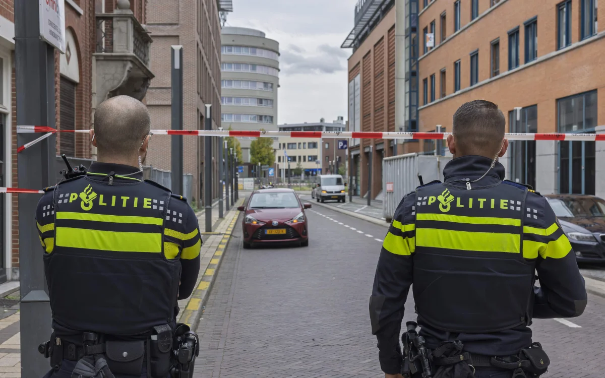 Deux policiers en uniforme bleu foncé à bandes jaunes se tiennent près d'une barrière, surveillant une rue restreinte aux Pays-Bas.