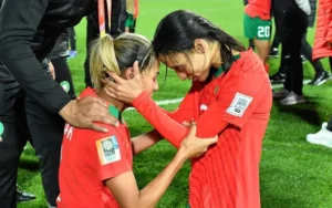 Des footballeuses marocaines partagent un moment émouvant sur le terrain, célébrant une victoire en Coupe d'Afrique, vêtues de tenues rouges.