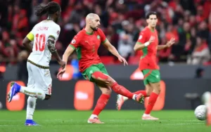 Morocco's Sofyan Amrabat strikes the ball in a vibrant match against Senegal, highlighted by red and green team kits and intense gameplay.