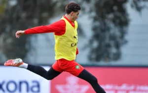 لاعب مغربي يرتدي صدرية تدريب صفراء يؤدي ركلة ديناميكية، يظهر مهارة وخفة حركة خلال جلسة تدريب.