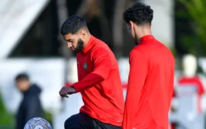 Des joueurs marocains en tenue d'entraînement rouge se concentrent sur un ballon lors d'une séance d'entraînement avant la Coupe d'Afrique.