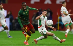 Morocco's player #13 attempts to control the ball against Cameroon’s #2 during an intense African Cup match, showcasing vibrant team kits.