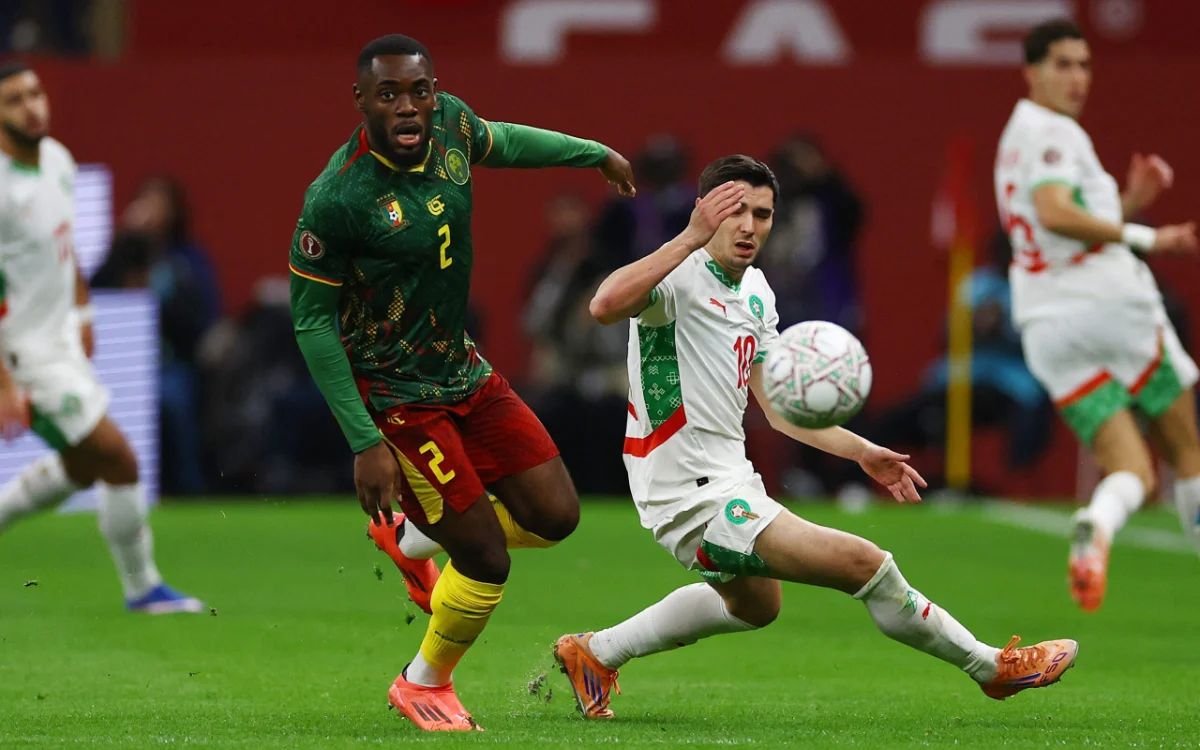 Morocco's player #13 attempts to control the ball against Cameroon’s #2 during an intense African Cup match, showcasing vibrant team kits.