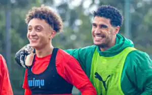 Moroccan football players share a light moment during training, showcasing smiles and camaraderie in red and green kits.