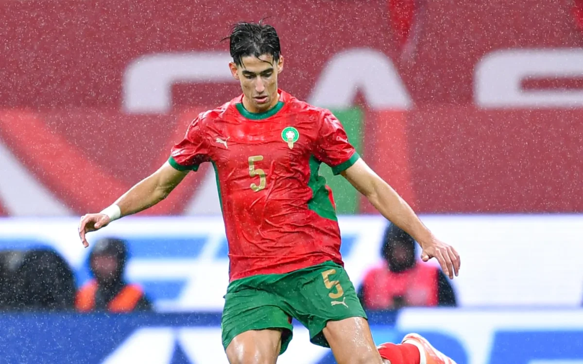 Moroccan defender in a vibrant red and green kit, poised for action amidst rainfall during a competitive match.