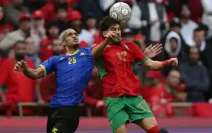 Moroccan player in red (17) heads the ball against Tanzanian player in blue (25) during an intense AFCON 2025 match.