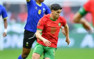 Un joueur marocain en maillot rouge avec des bordures vertes, numéro 10, dribble le ballon lors du match de la Coupe d'Afrique contre le Cameroun.