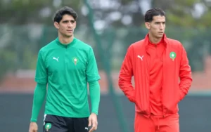 Joueurs marocains en tenue d'entraînement : l'un portant un haut vert et l'autre un survêtement rouge, tous deux affichant la fierté de l'équipe nationale.