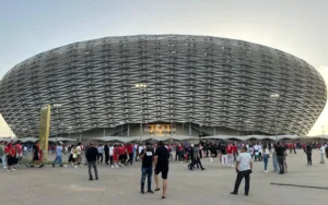 حشود تتجمع خارج ملعب عصري، مزين بالألوان الأحمر والأبيض، في انتظار مباريات كأس أمم إفريقيا 2025 بشغف.