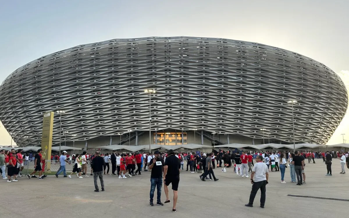 حشود تتجمع خارج ملعب عصري، مزين بالألوان الأحمر والأبيض، في انتظار مباريات كأس أمم إفريقيا 2025 بشغف.