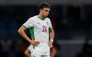 Neil El Aynaoui in Morocco's white kit with green accents, looking pensive during a match, reflects the intensity of competition.