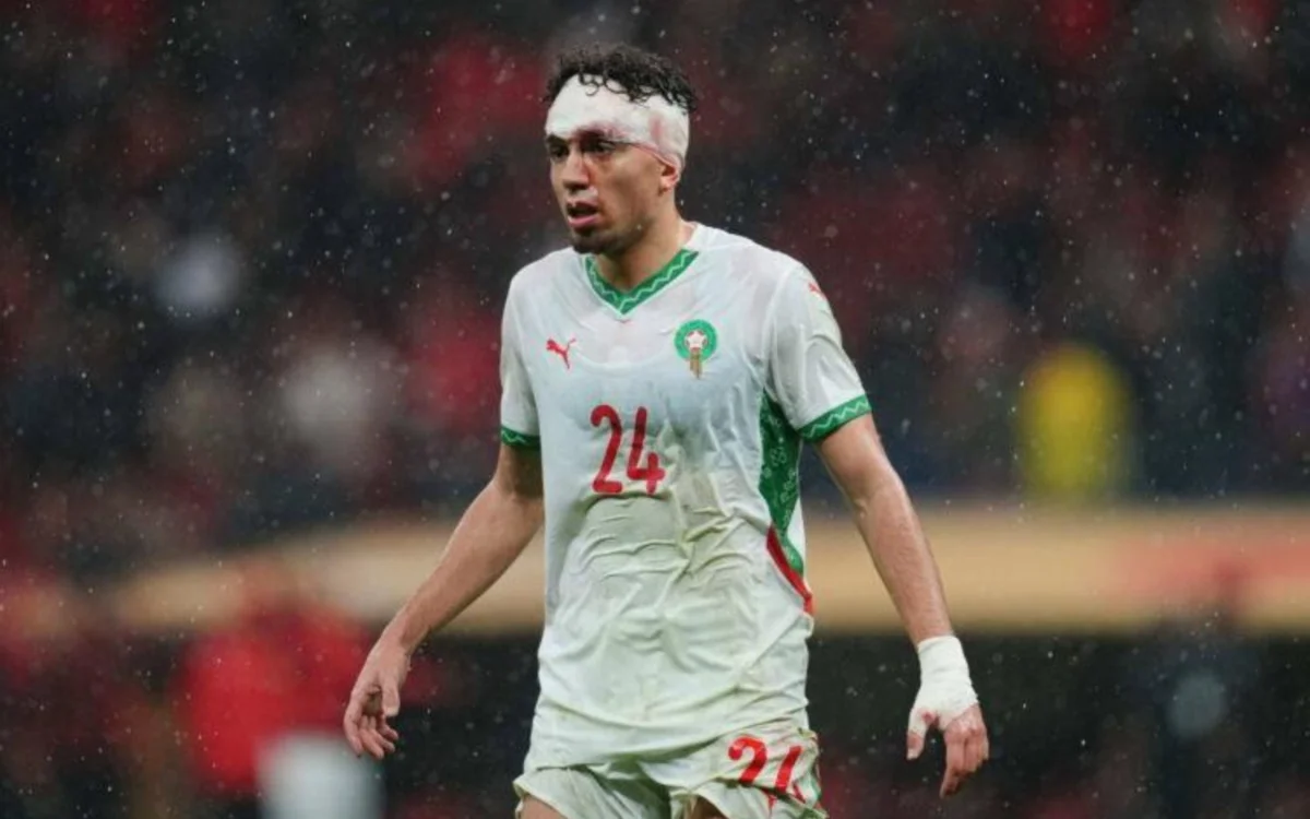 Neil El Aynaoui in Morocco's white kit, number 24, walks through rain, showing signs of battle with a bandaged head and determined expression.
