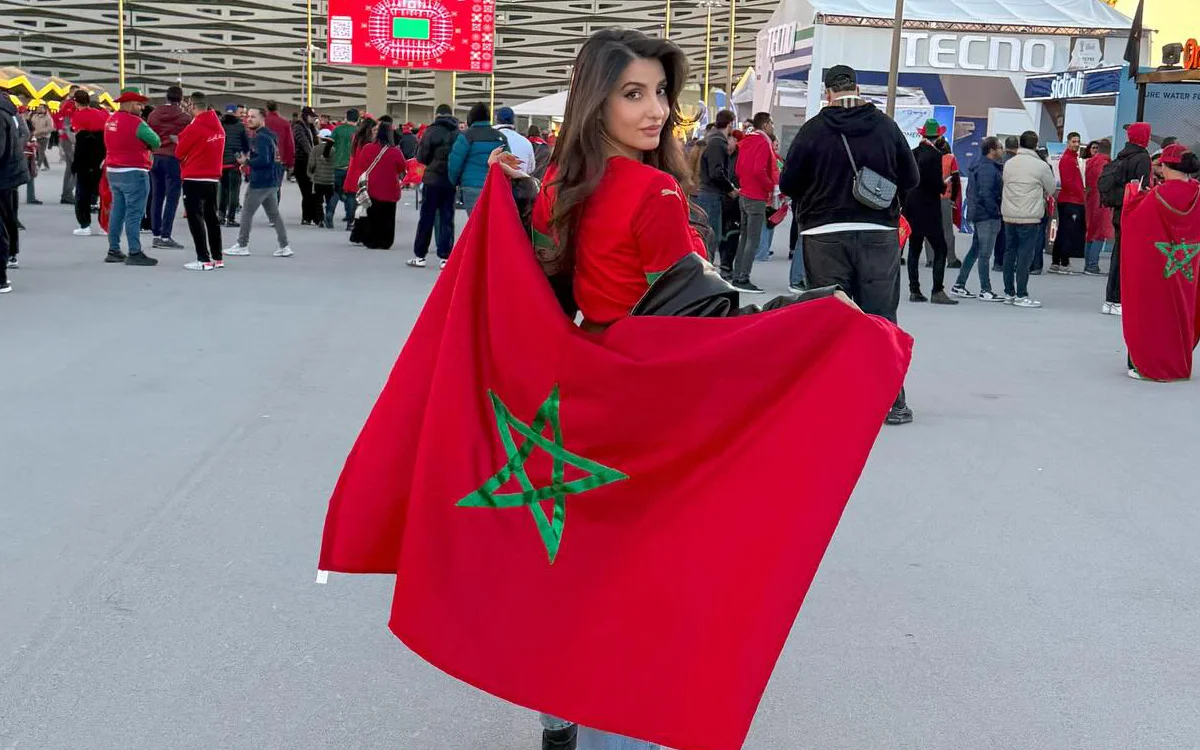 Un supporter marocain brandit fièrement le drapeau national orné d'une étoile verte au sein d'une foule animée, en célébration à l'extérieur du stade pendant un match.