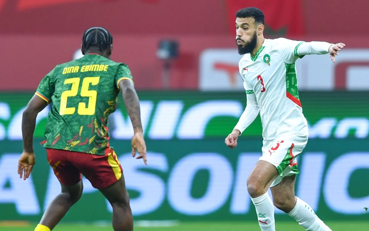 Noussair Mazraoui en tenue blanche et verte du Maroc défend contre Dina Ebimbe du Cameroun, qui porte un maillot vert vif avec des accents rouges.