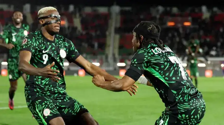 Ousim Loukman célèbre avec un coéquipier après avoir marqué lors d'un match, tous deux portant le maillot vert vif du Nigeria devant une foule en liesse.