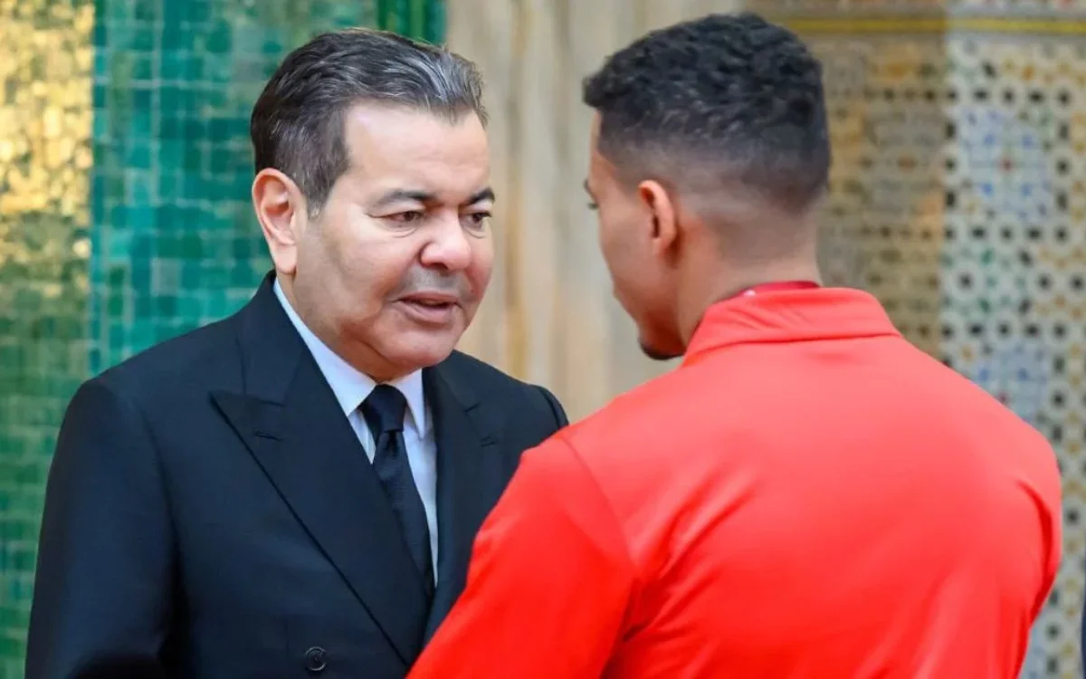 Prince Moulay Rachid converses with a Moroccan player in red, set against a backdrop of intricate Moroccan mosaic tiles.