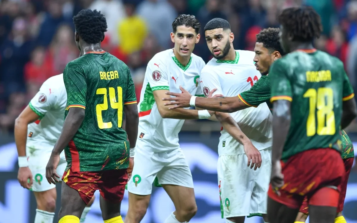 Morocco players in white jerseys discuss with Cameroon opponents in green during a tense moment in their recent match.