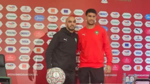 وليد الركراكي وياسين بونو يلتقيان صورة مع كرة قدم في مؤتمر صحفي لكأس الأمم الأفريقية 2025، على خلفية تحمل شعارات الرعاة.