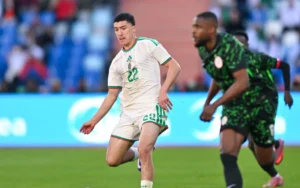 Le joueur numéro 22 de l'Algérie dribble le ballon contre le Nigeria, mettant en valeur les couleurs de l'équipe vert et blanc dans un cadre de match compétitif.