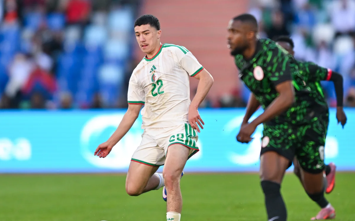 Le joueur numéro 22 de l'Algérie dribble le ballon contre le Nigeria, mettant en valeur les couleurs de l'équipe vert et blanc dans un cadre de match compétitif.