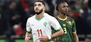 Morocco's player wearing jersey number 11, with a white and green kit, looks up thoughtfully as a Cameroonian player in green stands nearby.