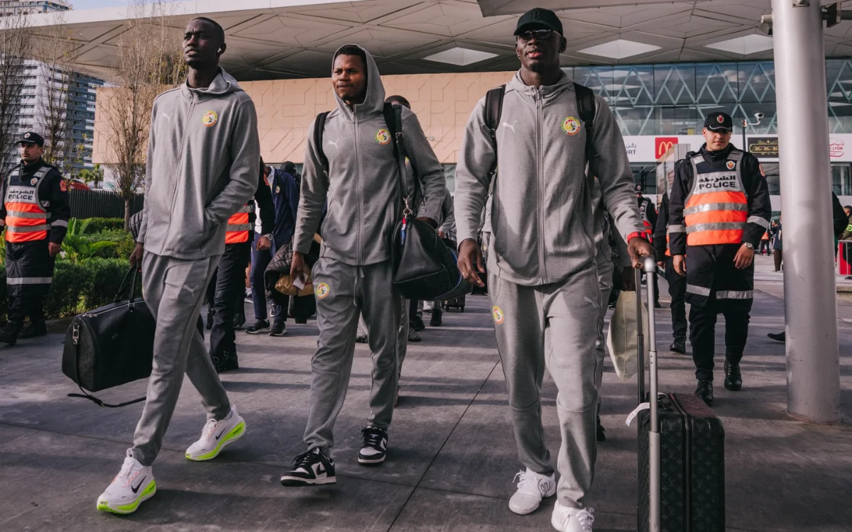 Senegalese football players in grey tracksuits arrive at the airport, accompanied by security personnel, ahead of the Africa Cup.