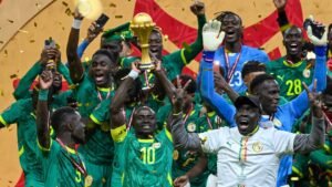 Les joueurs sénégalais célèbrent avec le trophée africain, vêtus de tenues vertes et de médailles, au milieu des confettis et avec des expressions joyeuses.