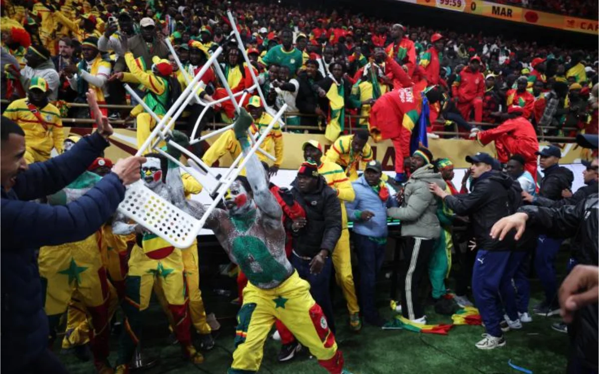 Fan chaos at the Africa Cup, featuring Senegalese supporters in vibrant yellow and green, with one holding a chair amidst a crowded stadium.