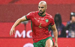 Sofyan Amrabat in het rode tenue van Marokko, nummer 4, sprint over het veld tijdens een wedstrijd en toont vastberadenheid en focus.