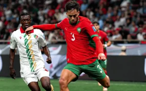 Souffian El Karouani, vêtu du maillot rouge du Maroc, défie un adversaire lors d'une action de jeu dynamique pendant un tournoi international.