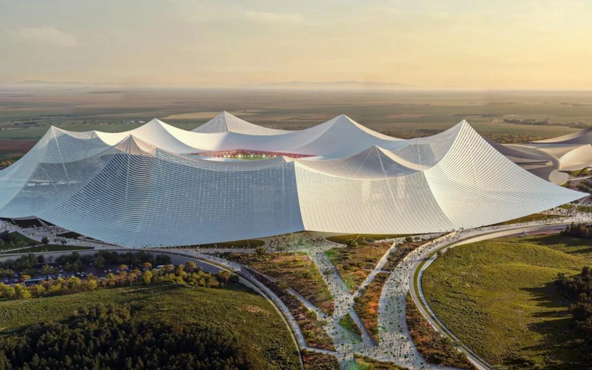 Futuristic stadium design for the 2030 World Cup, featuring undulating white roofs, surrounded by greenery and crowds.