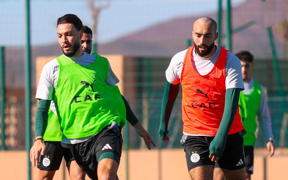 Les joueurs algériens en gilets d'entraînement verts et oranges s'exercent sur un terrain ensoleillé, se concentrant sur le travail d'équipe avant les prochains matchs.