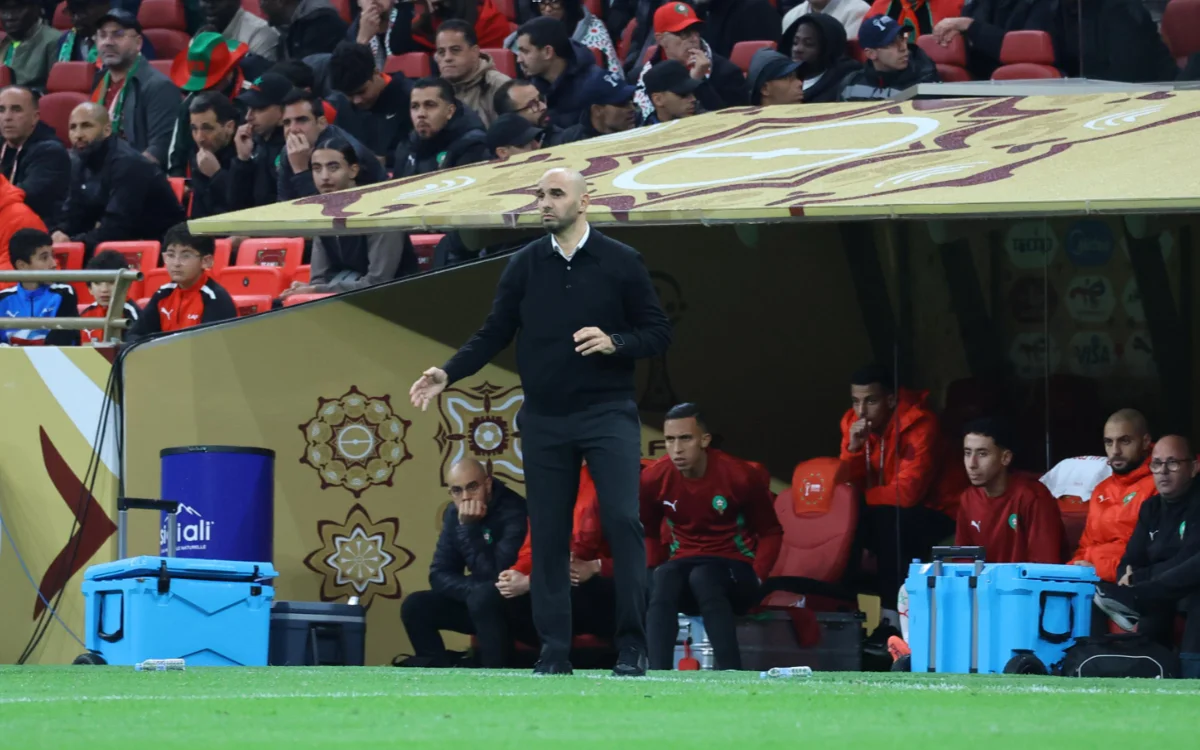 Walid Regragui gestures from the sidelines during a match, with Moroccan players and fans in the background, showcasing team spirit.