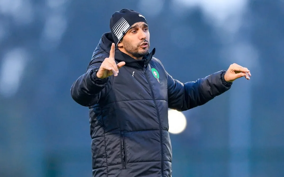 Walid Regragui gebaart gepassioneerd tijdens coaching, gekleed in een zwart jasje en muts, wat zijn toewijding aan het Marokkaanse voetbal benadrukt.