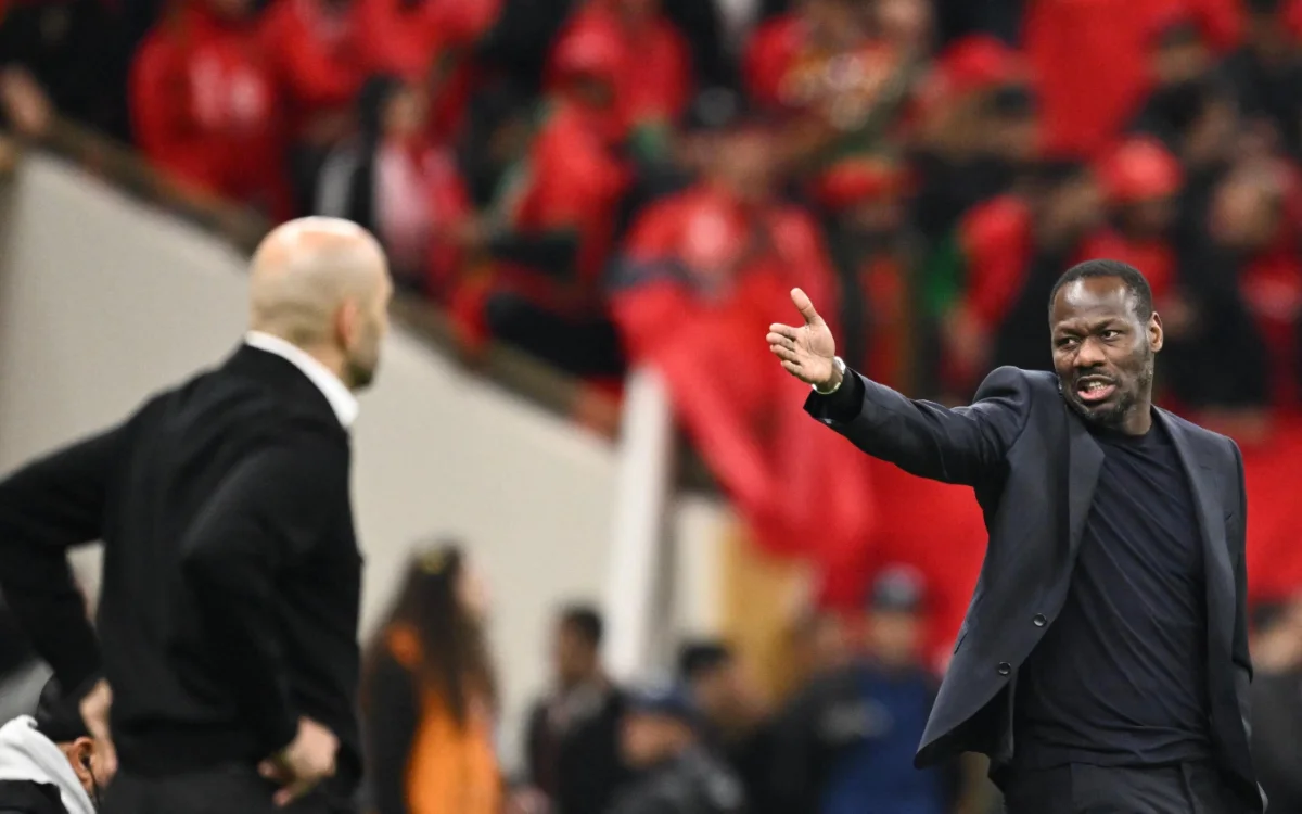 وليد الركراكي يشير بحماس نحو الملعب بينما يتجمع خلفه حشد من المشجعين المغاربة مرتدين اللون الأحمر، بينما يخوض فريقه نهائي كأس إفريقيا.