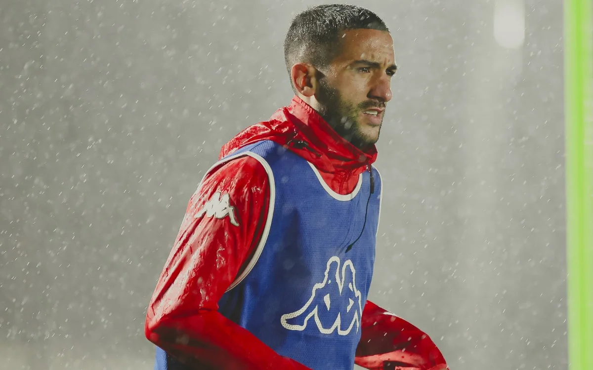 Hakim Ziyech traint in zware regen, draagt een blauw Kappa-trainingsvest over een rood jasje, wat zijn focus en vastberadenheid benadrukt.