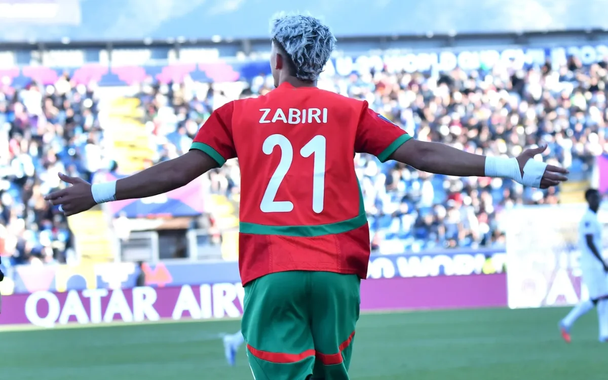 Yassir Zabiri célèbre les bras grands ouverts, portant le maillot vert et rouge de l'équipe nationale marocaine, numéro 21, dans une atmosphère vibrante du stade.