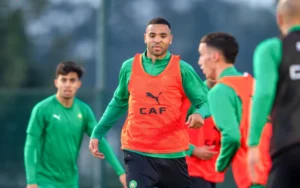 Youssef En-Nesyri trains with the Moroccan national team, wearing an orange bib, amidst teammates in green kit during a training session.
