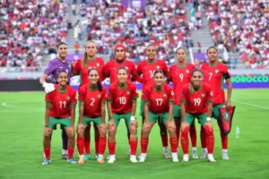 Morocco's women's national football team poses together in vibrant red and green kits, with a stadium crowd in the background.