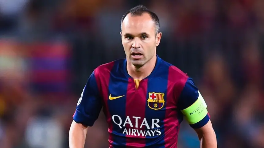 Andrés Iniesta in a maroon and blue Barcelona kit, captaining the team during a match, focused and determined on the pitch.