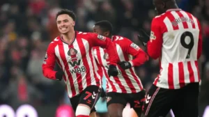 Sunderland players celebrate a goal, featuring a smiling player in a red and white striped jersey, with team logo visible.
