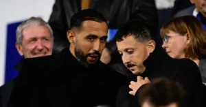 Badr Hari and Hakim Ziyech in a dark jacket conversation at a football match, surrounded by spectators, highlighting Moroccan presence.